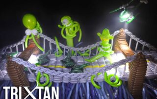 Balloon sculpture scene featuring aliens attacking a bridge with tanks and helicopters, all made from balloons and lit with dramatic lighting