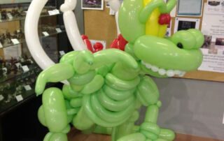 Green balloon dragon sculpture with wings and yellow claws on display at a game and hobby shop