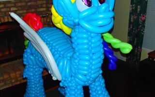 Large Rainbow Dash balloon sculpture with blue body, rainbow mane, and white wings, displayed indoors